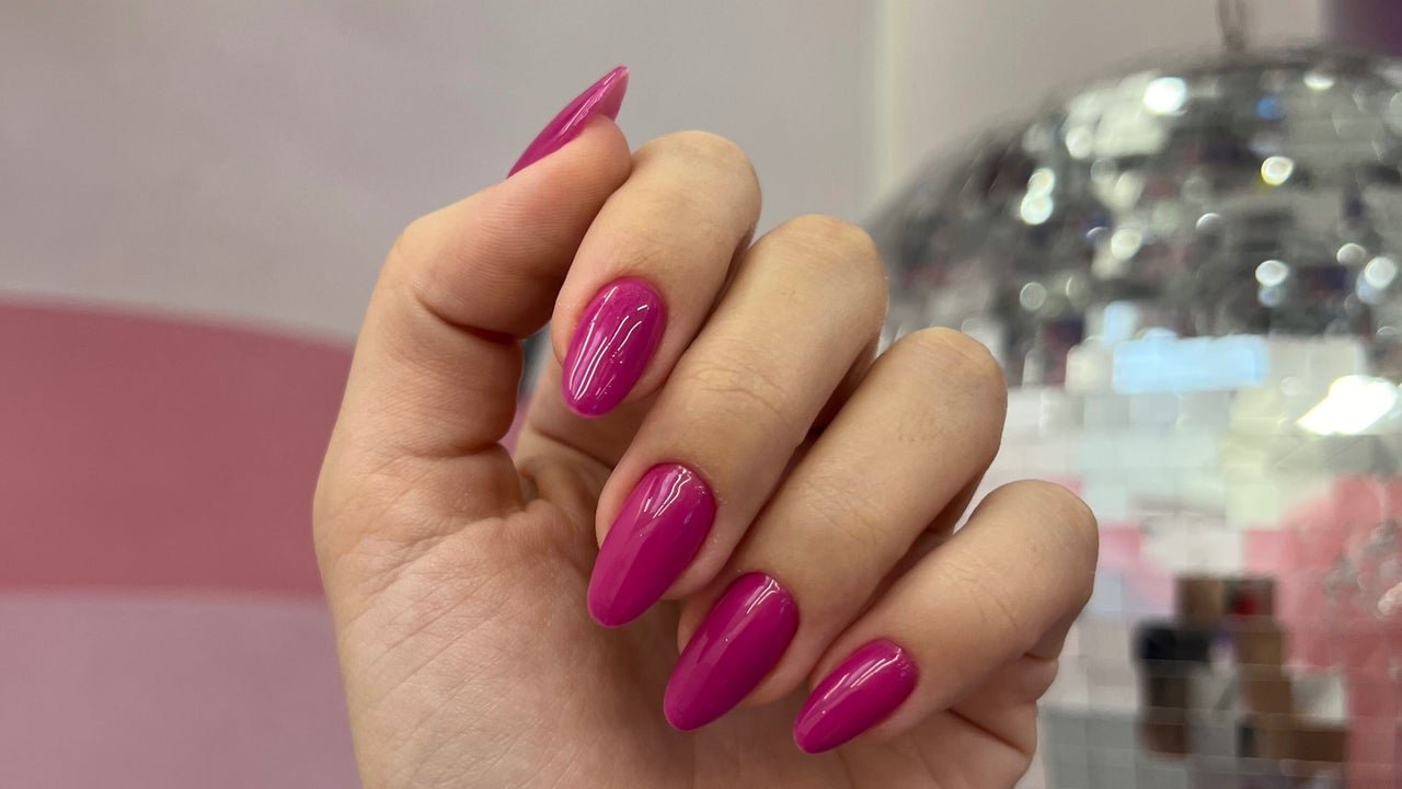 Hand met felroze amandelnagels voor de roze muur en de spiegelbal in de studio