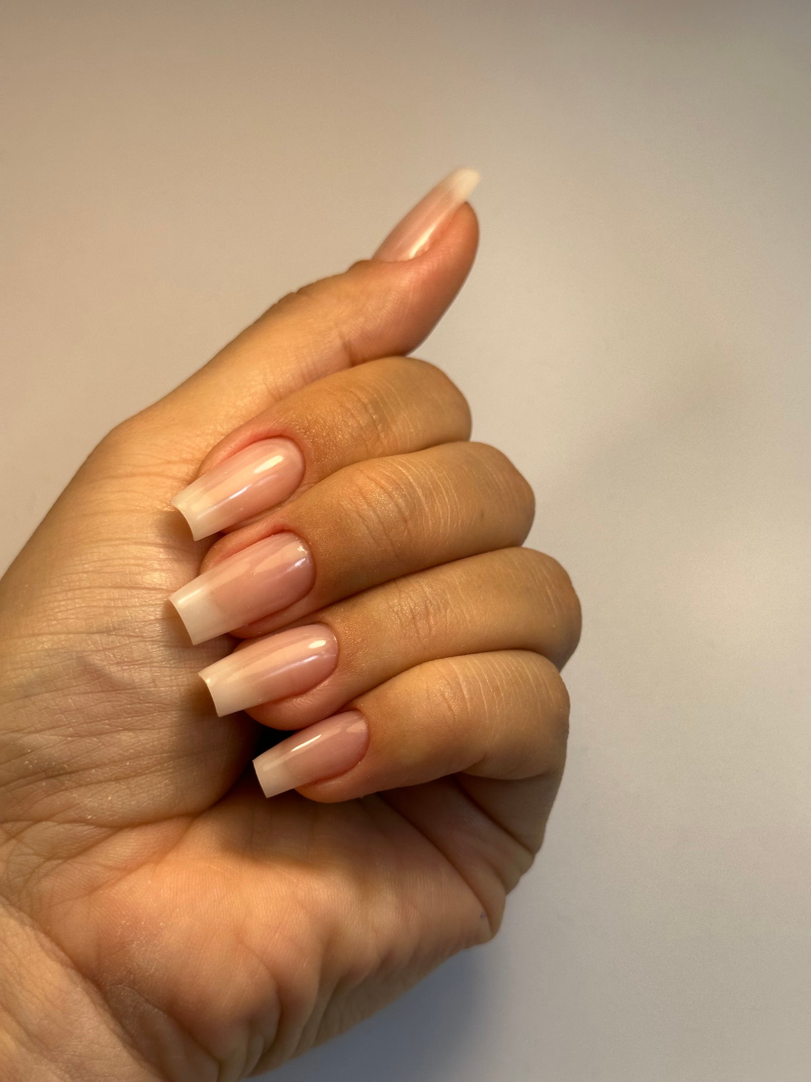 Hand met een nieuwe set naturel nude nagels in een vierkante vorm